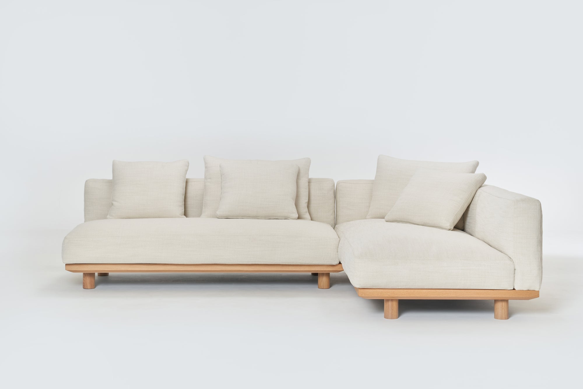 The Islet Modular Sofa | Fabric • M3 by Wooden Stories is a modern L-shaped beige sofa with a wooden base, four matching cushions, and a minimalist design, shown against a plain white background.