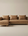 The Islet Modular Sofa | Leather • M3 by Wooden Stories, an L-shaped sectional with light brown upholstery and matching cushions, sits on a light beige floor against a neutral wall.