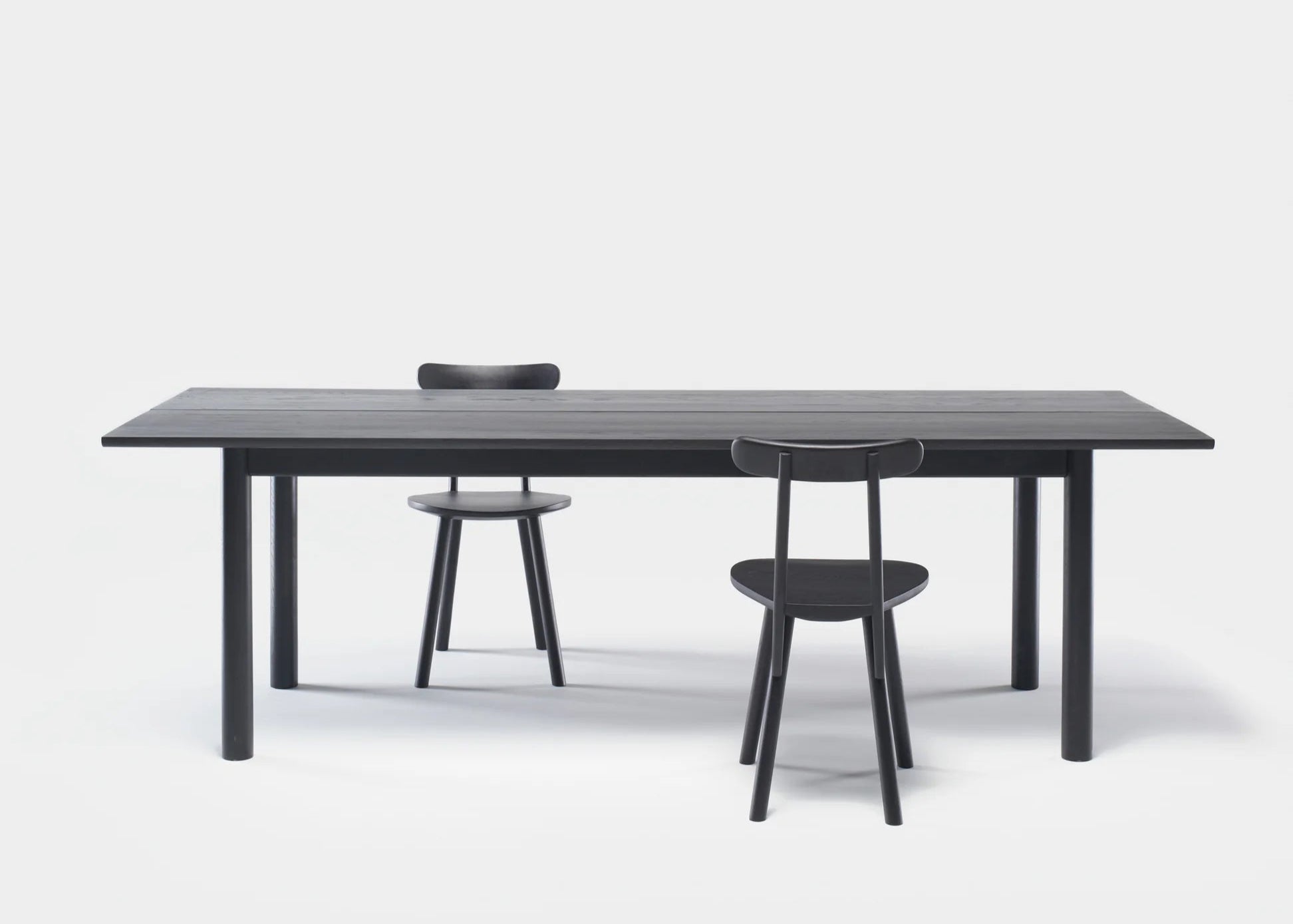 The Itamae Dining Table | Black Oak by Wooden Stories, featuring a solid oak tabletop and four legs, is paired with two matching black chairs against a plain white background.