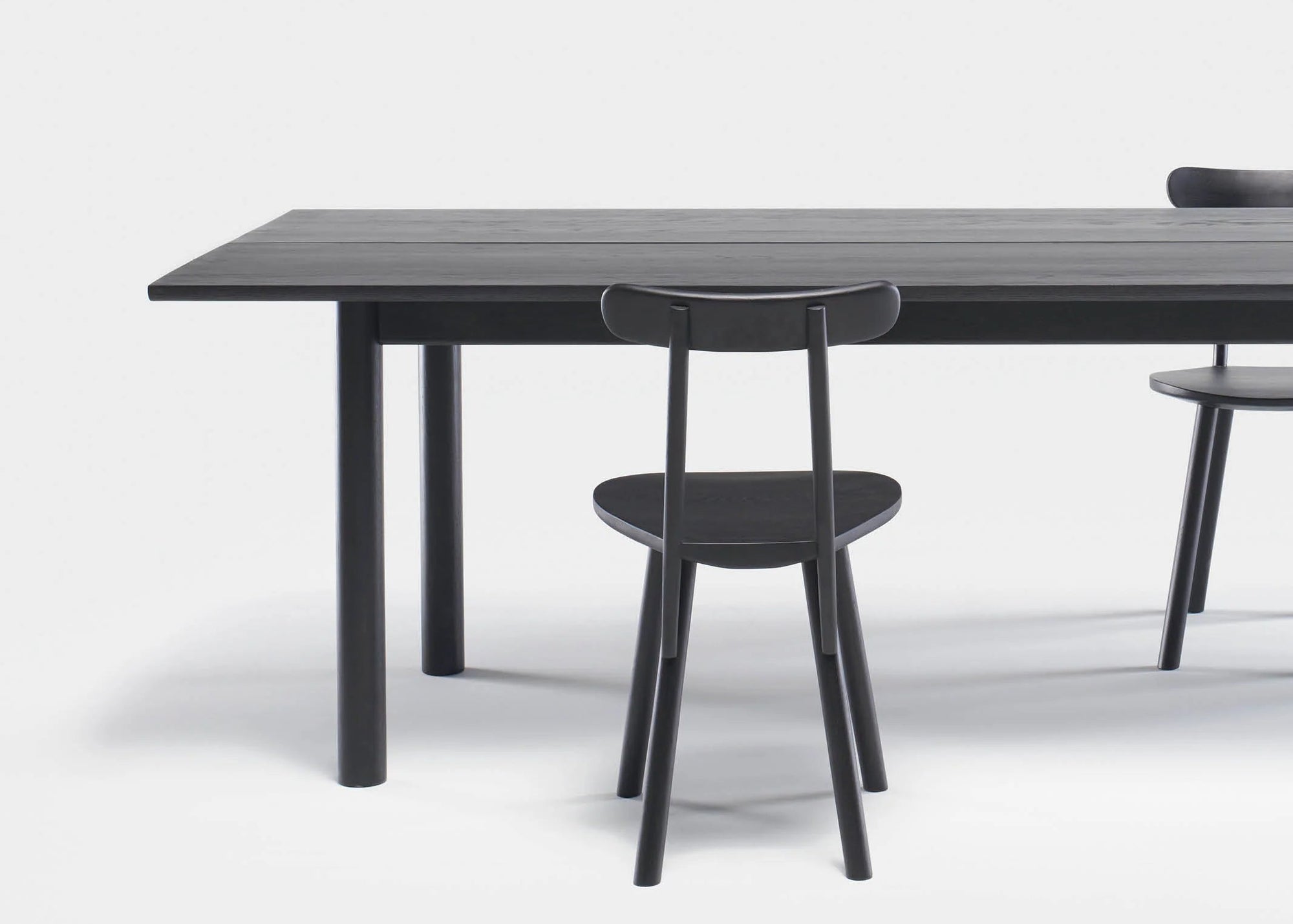 The Wooden Stories Itamae Dining Table in black oak, with cylindrical legs and a matching chair set, is partially visible against a plain white background.