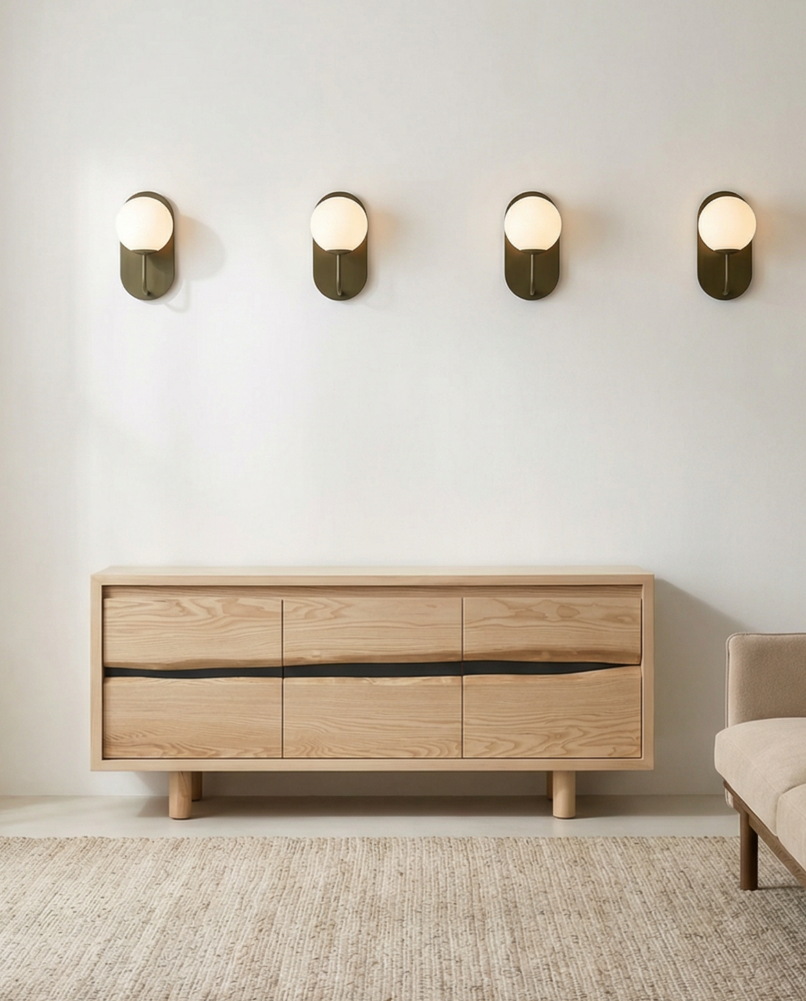 A minimalist living room features the SOBU Jupiter Sideboard - White Ash 64", a beige rug, neutral walls, four modern wall sconces with round bulbs, and part of a beige sofa visible on the right.