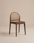 The Wooden Stories Luk Dining Chair | Fabric Seat features a cane weave rattan backrest and a brown cushioned seat, displayed against a plain beige background.
