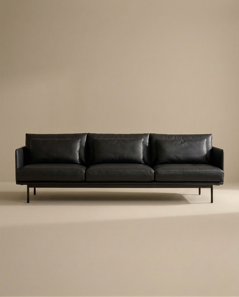 The SOBU Cherry Sofa | Leather features slim armrests, Danish lines, metal legs, and black leather upholstery. Its minimalist design fits perfectly in modern spaces, shown here against a plain beige background.