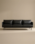 The SOBU Cherry Sofa | Leather features slim armrests, Danish lines, metal legs, and black leather upholstery. Its minimalist design fits perfectly in modern spaces, shown here against a plain beige background.