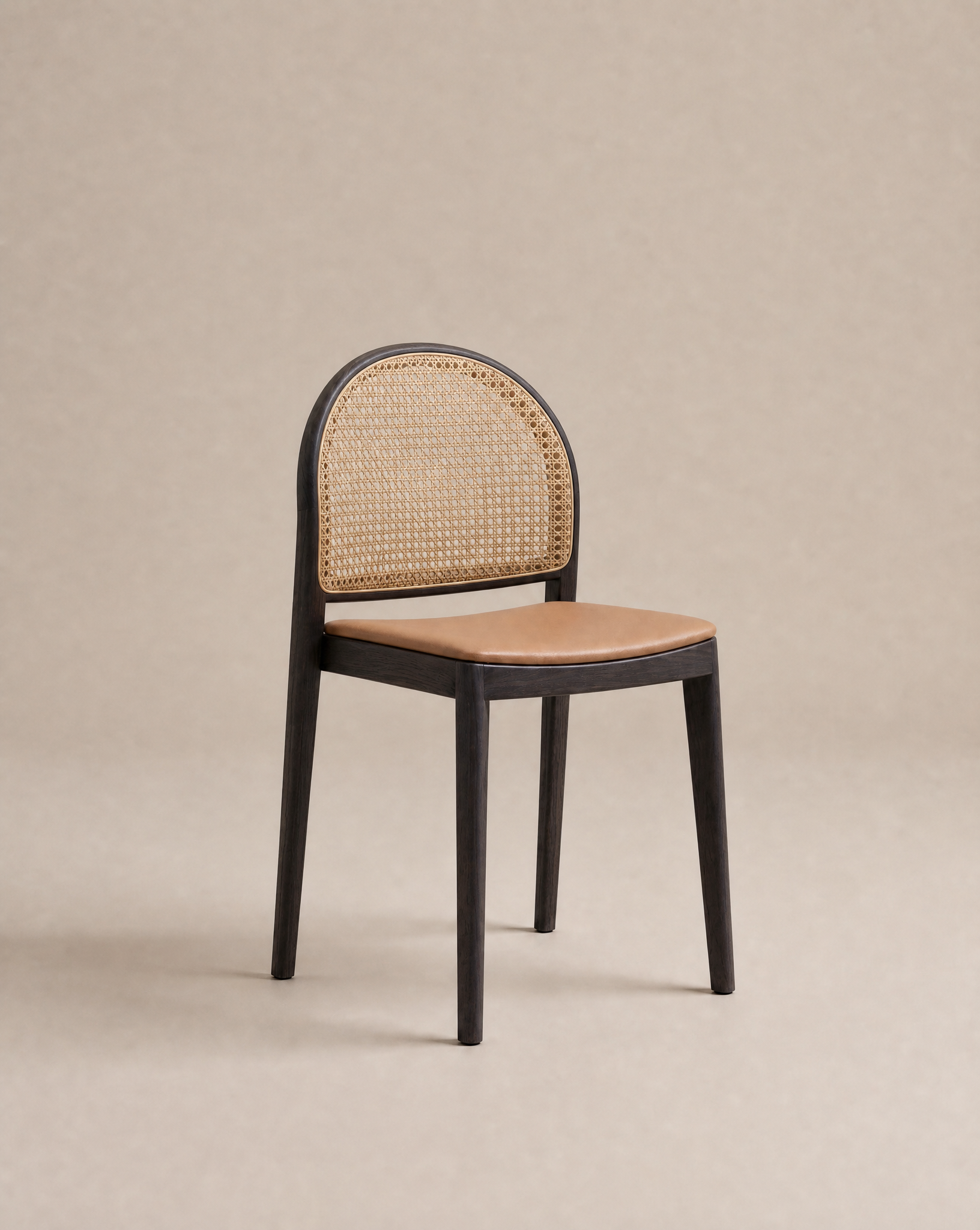 The Luk Dining Chair by Wooden Stories features a black wooden frame, curved cane weave rattan backrest, and light brown leather or faux leather seat, shown against a plain beige background.