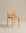 The Luk Dining Chair by Wooden Stories features a rounded cane weave rattan backrest and a light brown leather seat, shown against a plain beige background.