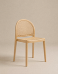The Luk Dining Chair by Wooden Stories features a light wooden arch silhouette, rounded backrest, and woven cane seat. Set against a beige background, its minimalist design and rattan details add modern, contract-grade style.