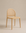 The Luk Dining Chair by Wooden Stories features a light wooden arch silhouette, rounded backrest, and woven cane seat. Set against a beige background, its minimalist design and rattan details add modern, contract-grade style.