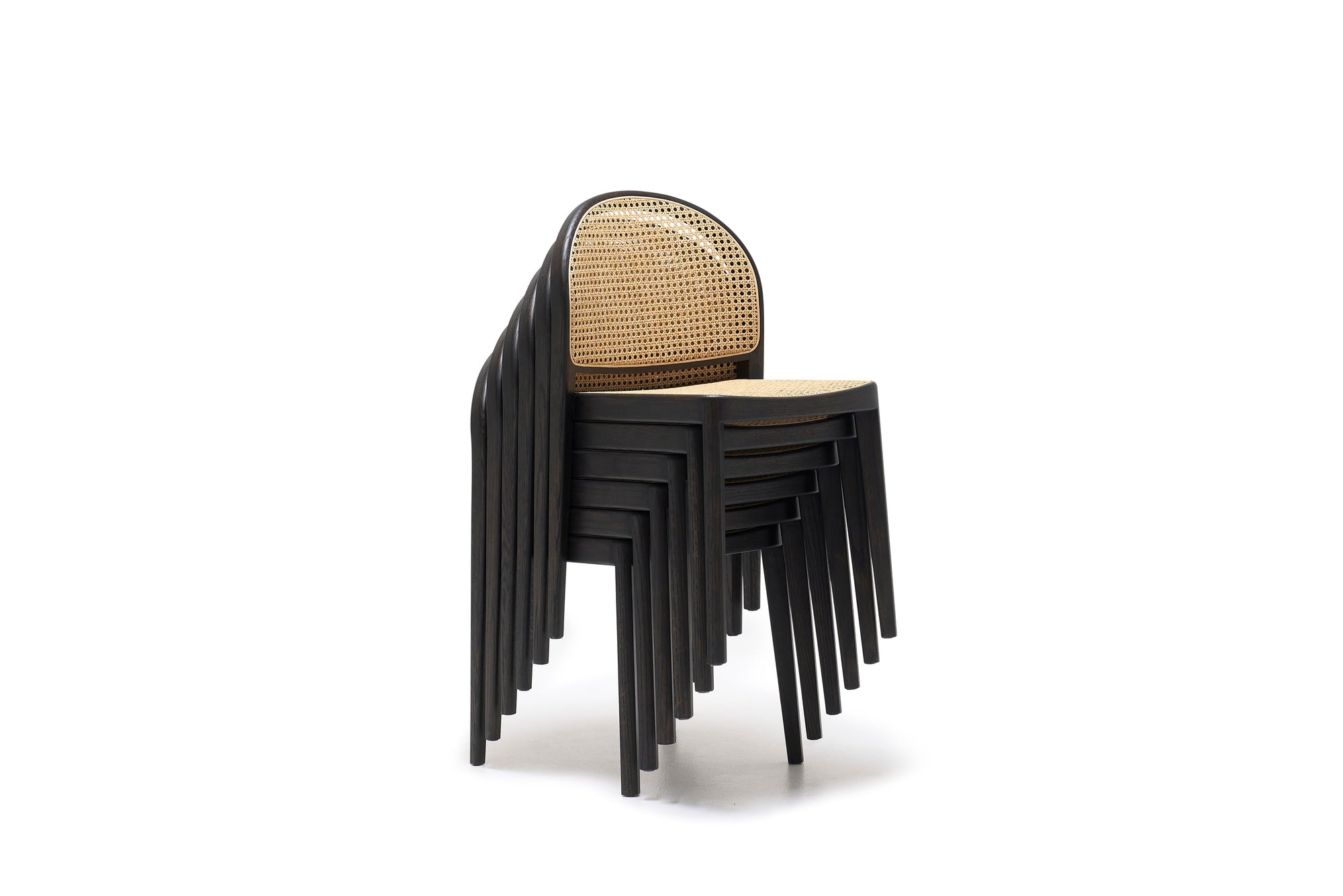 A stack of six contract-grade Wooden Stories Luk Dining Chairs with rounded backs and cane weave rattan seats, arranged neatly against a white background.