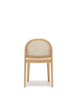 The Wooden Stories Luk Dining Chair features a simple, modern design with a rounded backrest and cane weave rattan seat, photographed front-facing on a white backdrop. This contract-grade chair combines style and durability for any space.