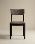The Noki Dining Chair by Wooden Stories features a modern, contract-grade black oak frame with a textured, upholstered seat and backrest in a brown and white pattern set against a neutral beige background.