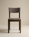 The Wooden Stories Noki Dining Chair features an espresso oak frame with cushioned seat and backrest in textured grayish fabric, shown against a plain beige background.