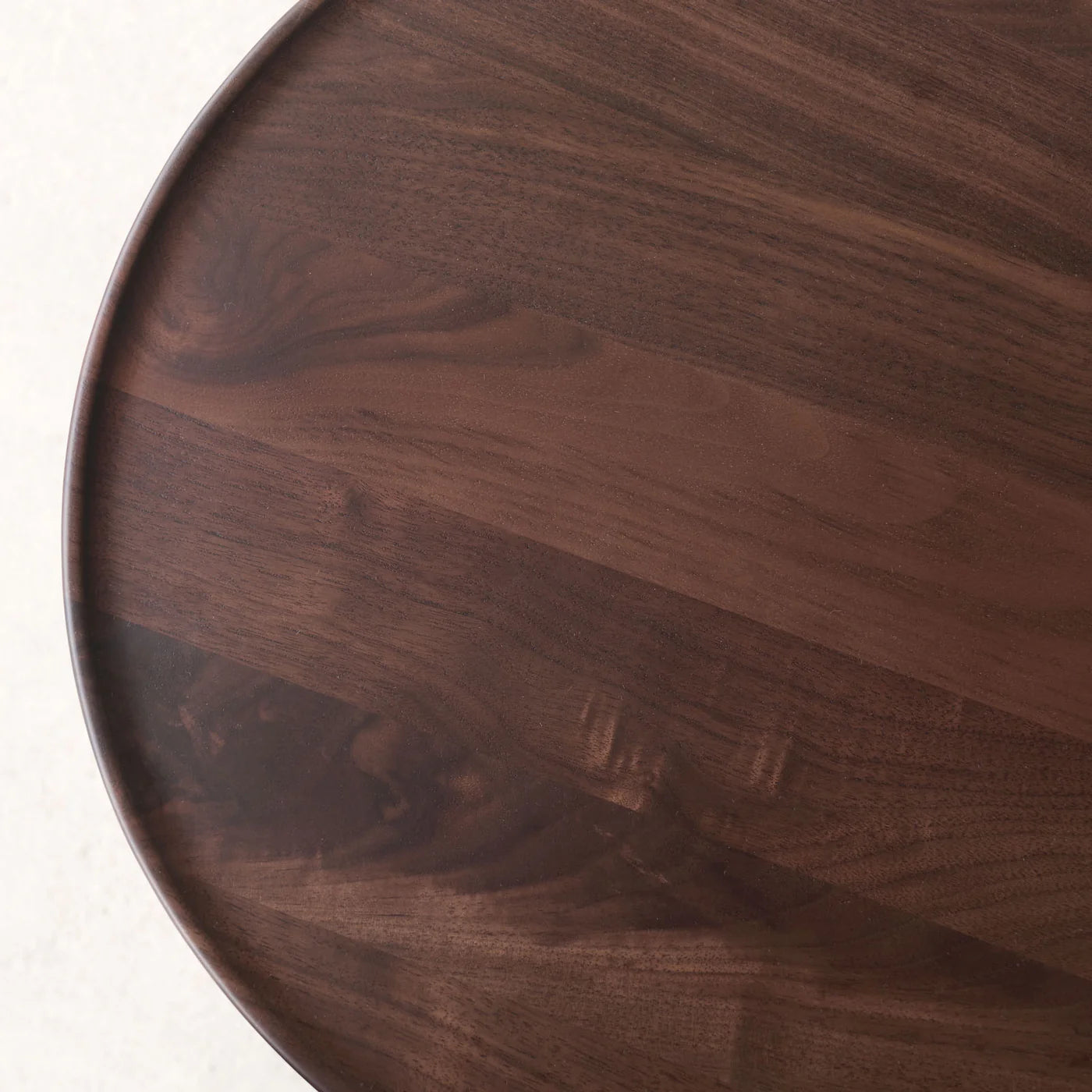 A close-up view of the Bystander Side Table by Wooden Stories, featuring a round, dark wood tabletop with a smooth finish and visible natural grain patterns.