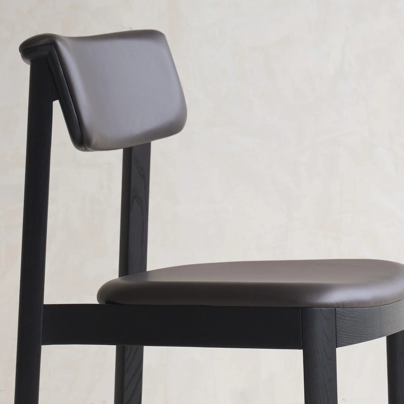 The Noki Dining Chair by Wooden Stories features a black oak frame and leather upholstery, set against a light textured backdrop—highlighting refined Japanese design aesthetics.