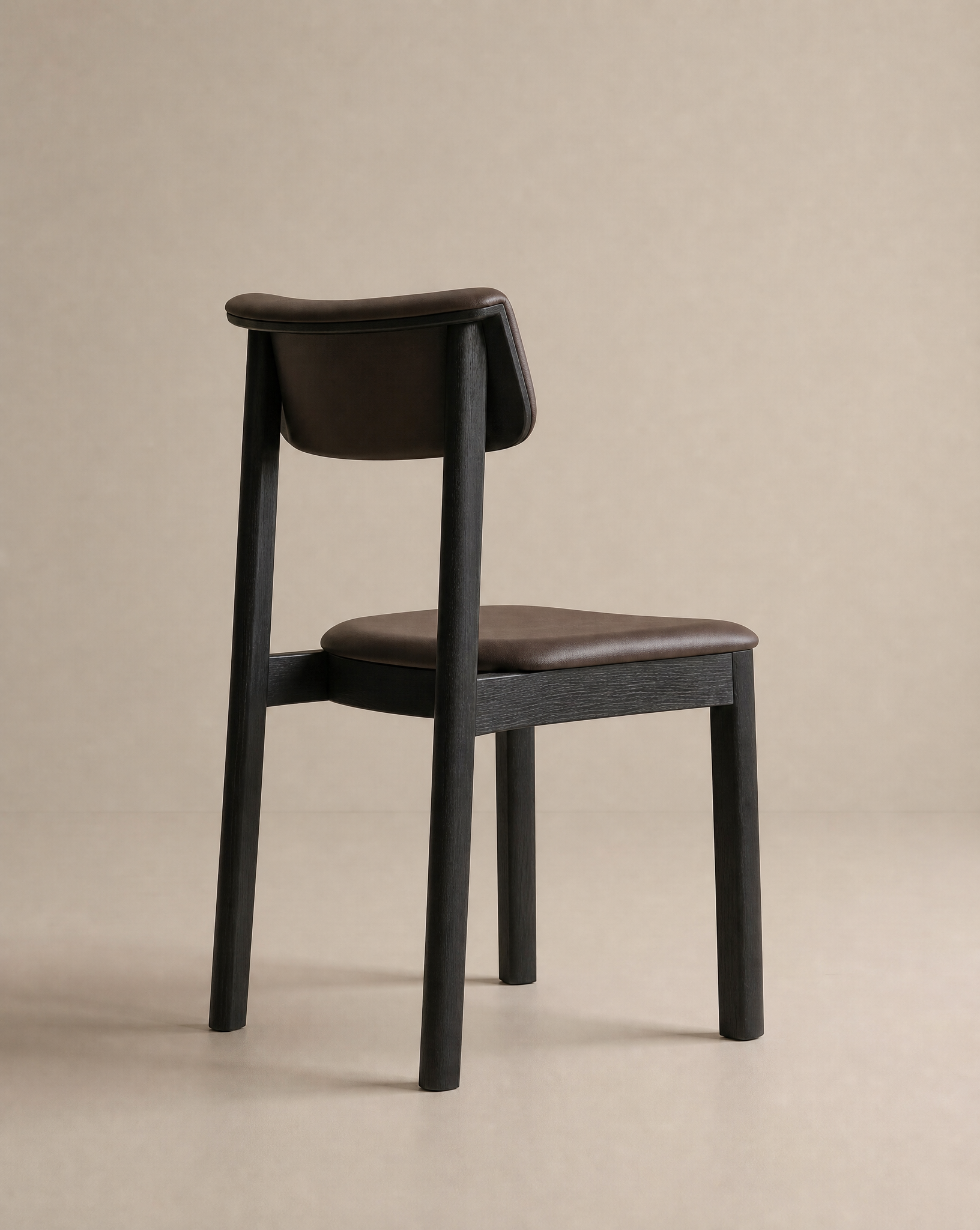 The Noki Dining Chair | Leather by Wooden Stories features solid wood construction and a dark brown leather cushioned seat and backrest, set at an angle against a plain beige background.