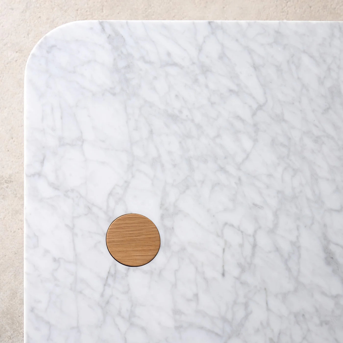 A close-up of the Pivot Coffee Table | Rectangular by Wooden Stories shows a honed marble tabletop with grey veining and a round, solid wood dowel inlay near the corner, set against a light, textured background.