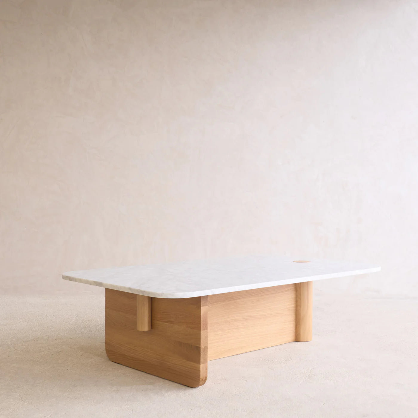 The Pivot Coffee Table | Rectangular - Stone &amp; Wood by Wooden Stories, featuring a white marble top and light wood base, sits in a softly lit room with beige walls and carpeting.