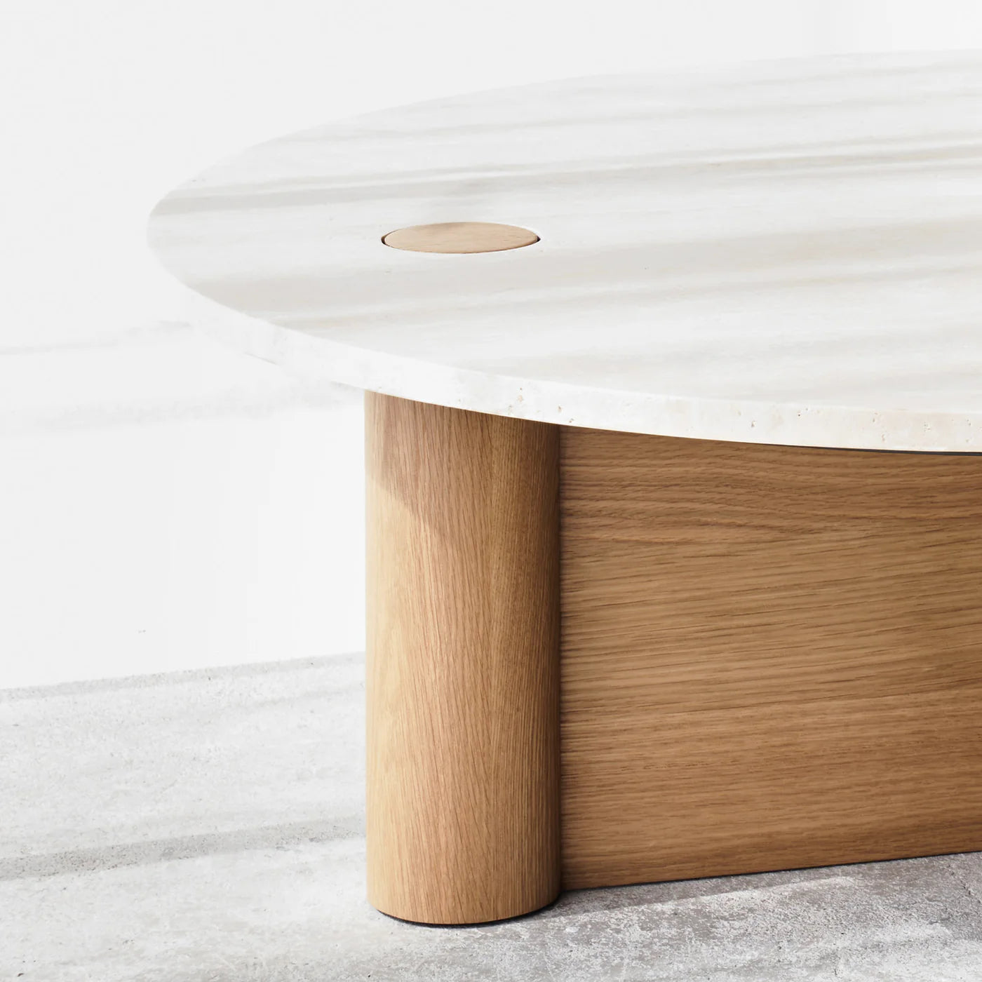 A close-up of the Wooden Stories Pivot Coffee Table - Light Oak, featuring a light honed marble top and cylindrical solid wood dowel legs, set on a light-colored floor with a small circular detail visible on the tabletop.
