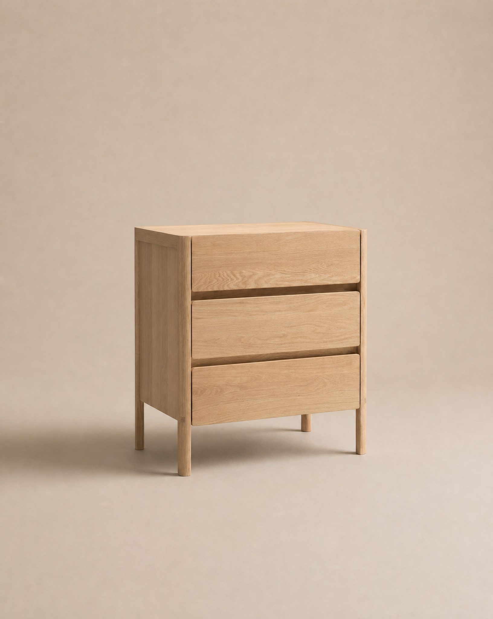 The Nell Tall Dresser by Wooden Stories, featuring a minimalist light wood design and three spacious drawers with premium metal runners for smooth operation, stands elegantly on four legs against a plain beige background, offering refined bedroom storage.