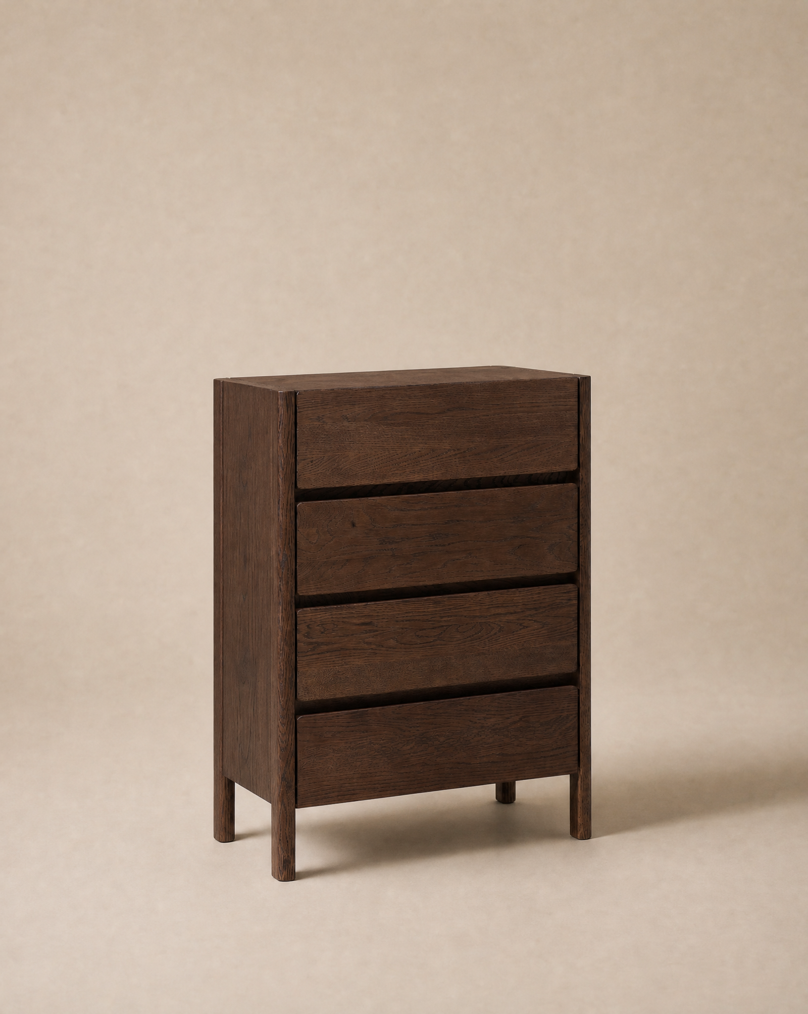 The Nell Tall Dresser by Wooden Stories stands on a beige background. Part of the Danish Collection, its simple, modern design features clean lines and no visible handles. Each of its three dark wood drawers glides smoothly on premium metal runners, making it an effortless bedroom storage solution.