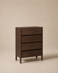 The Nell Tall Dresser by Wooden Stories stands on a beige background. Part of the Danish Collection, its simple, modern design features clean lines and no visible handles. Each of its three dark wood drawers glides smoothly on premium metal runners, making it an effortless bedroom storage solution.