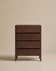 The Nell Tall Dresser by Wooden Stories stands against a plain beige background. Part of the elegant Danish Collection, this piece features a dark wood finish, three spacious drawers, and showcases simple, modern design with clean lines and a smooth surface. Perfect for bedroom storage, each drawer effortlessly glides open on premium metal runners.