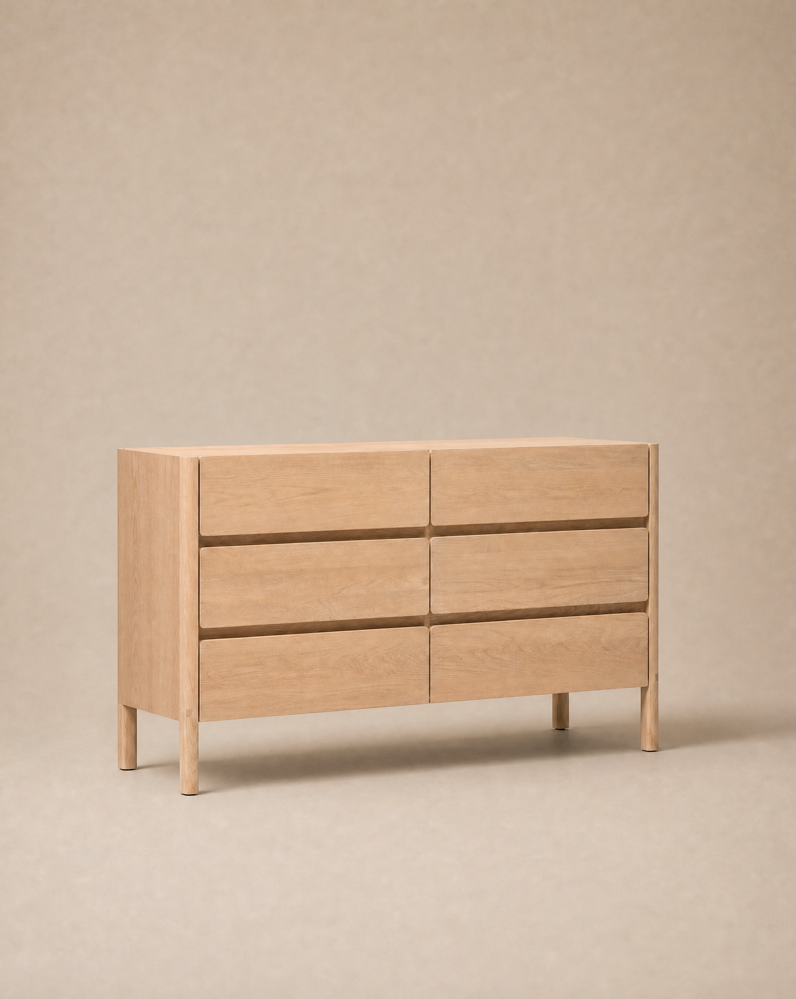 The Wooden Stories Nell Tall Dresser features six spacious drawers and is pictured against a neutral beige backdrop. As part of the Danish Collection, its modern, minimalist design showcases clean lines and a handleless silhouette. This dresser provides generous bedroom storage, crafted with premium metal runners to ensure smooth drawer operation.