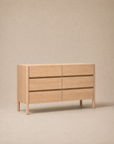 The Wooden Stories Nell Tall Dresser features six spacious drawers and is pictured against a neutral beige backdrop. As part of the Danish Collection, its modern, minimalist design showcases clean lines and a handleless silhouette. This dresser provides generous bedroom storage, crafted with premium metal runners to ensure smooth drawer operation.
