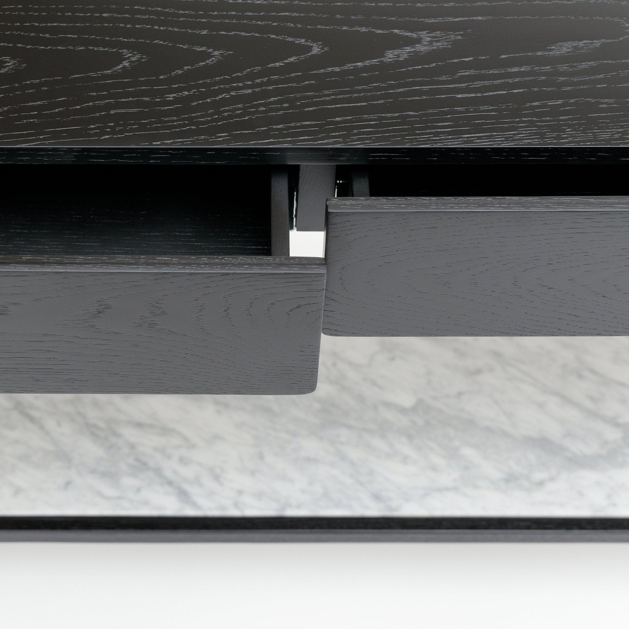 A close-up of the Nell Console by Wooden Stories, featuring a partially open black oak drawer with visible metal hardware, set above a stone surface.
