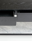 A close-up of the Nell Console by Wooden Stories, featuring a partially open black oak drawer with visible metal hardware, set above a stone surface.