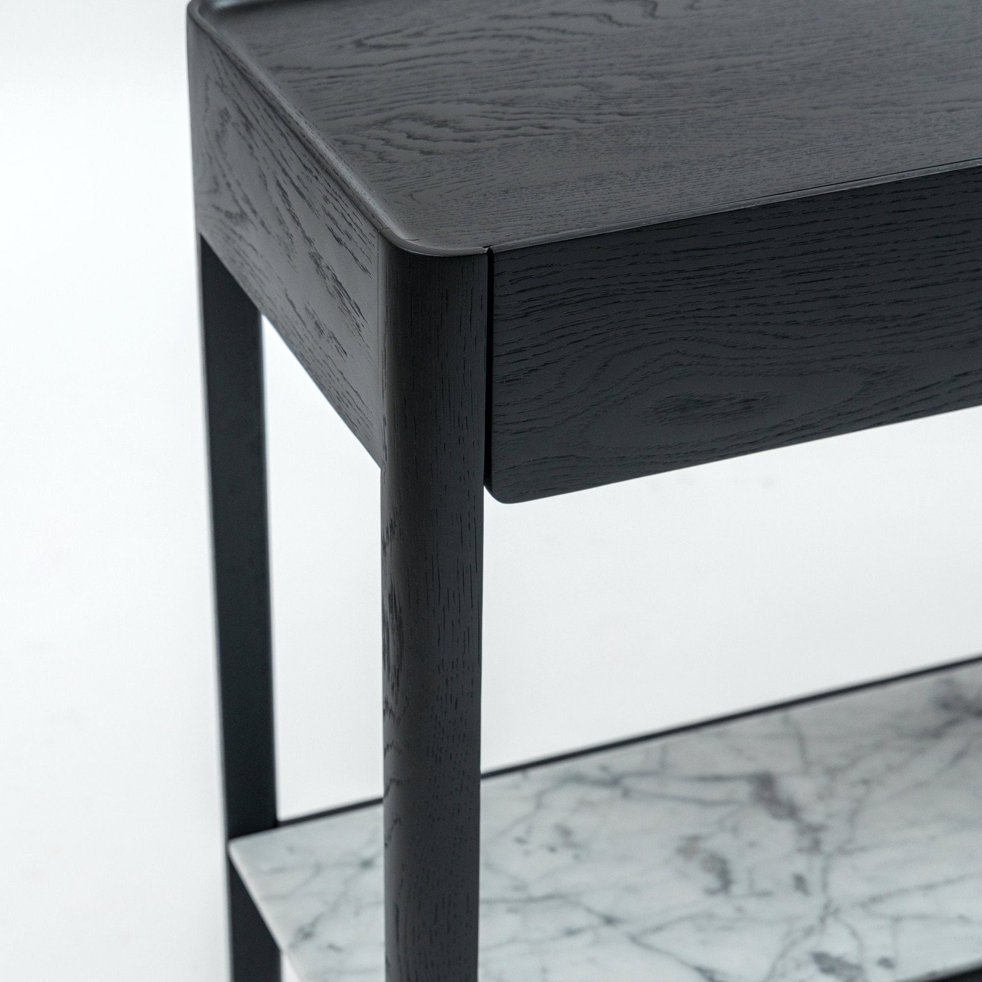 Close-up of the Wooden Stories Nell Console in black oak with rounded edges, a drawer, and a lower white marble shelf with gray veining, showcasing timeless Scandinavian style against a plain white background.