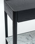 Close-up of the Wooden Stories Nell Console in black oak with rounded edges, a drawer, and a lower white marble shelf with gray veining, showcasing timeless Scandinavian style against a plain white background.