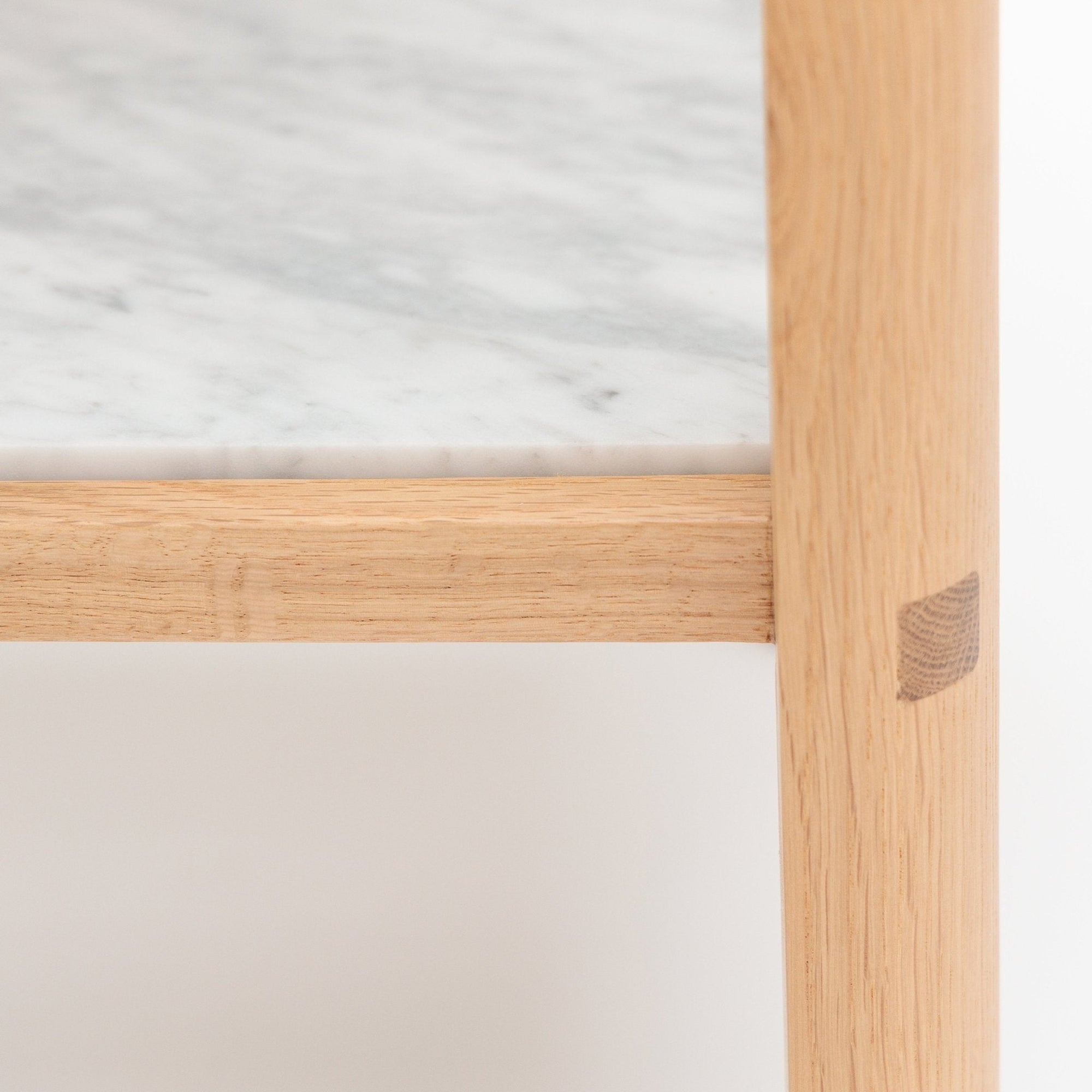 Close-up of the Nell Console by Wooden Stories, from the Danish collection. It features a light solid oak frame with a stone tabletop, highlighting its smooth joinery, wood texture, and a visible wooden patch on one leg.