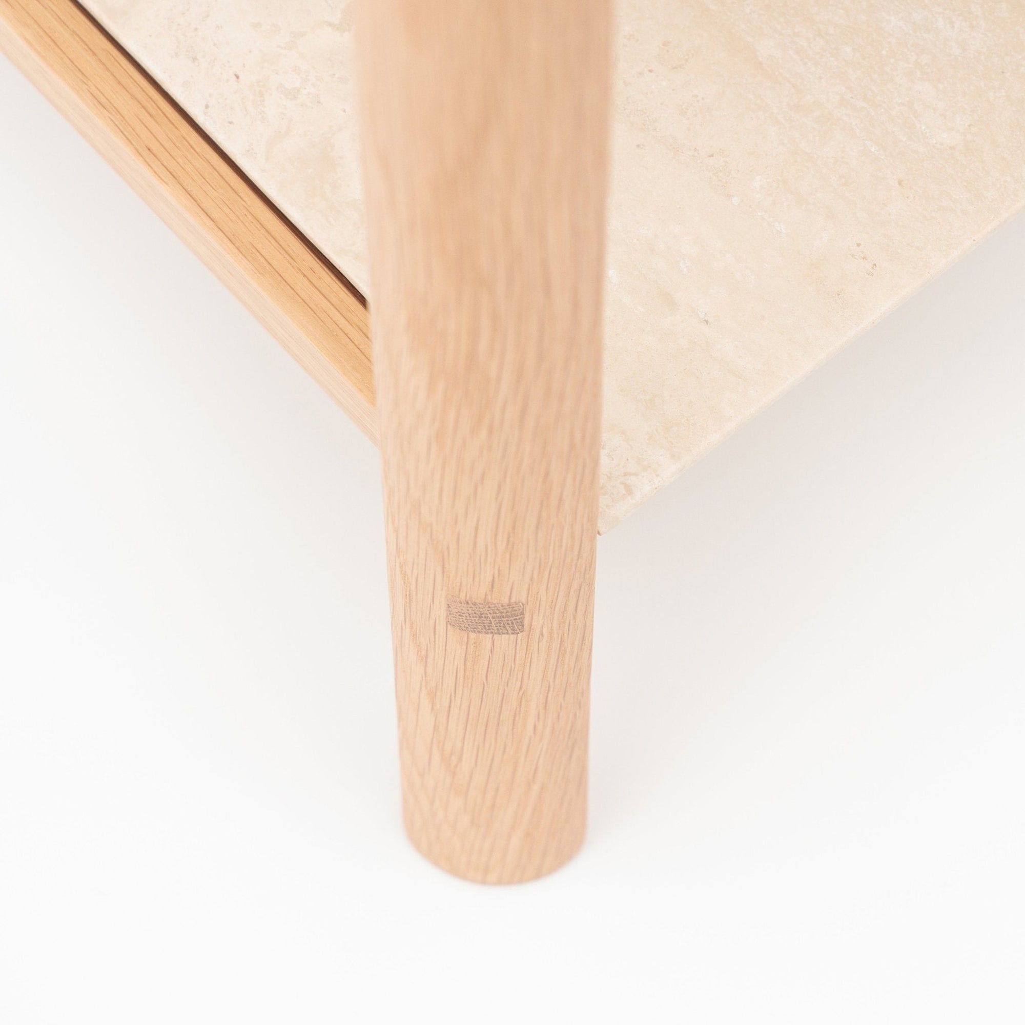 Close-up of the Nell Console by Wooden Stories, featuring a solid light oak leg with visible joint detail next to a beige stone tabletop, set against a white background.