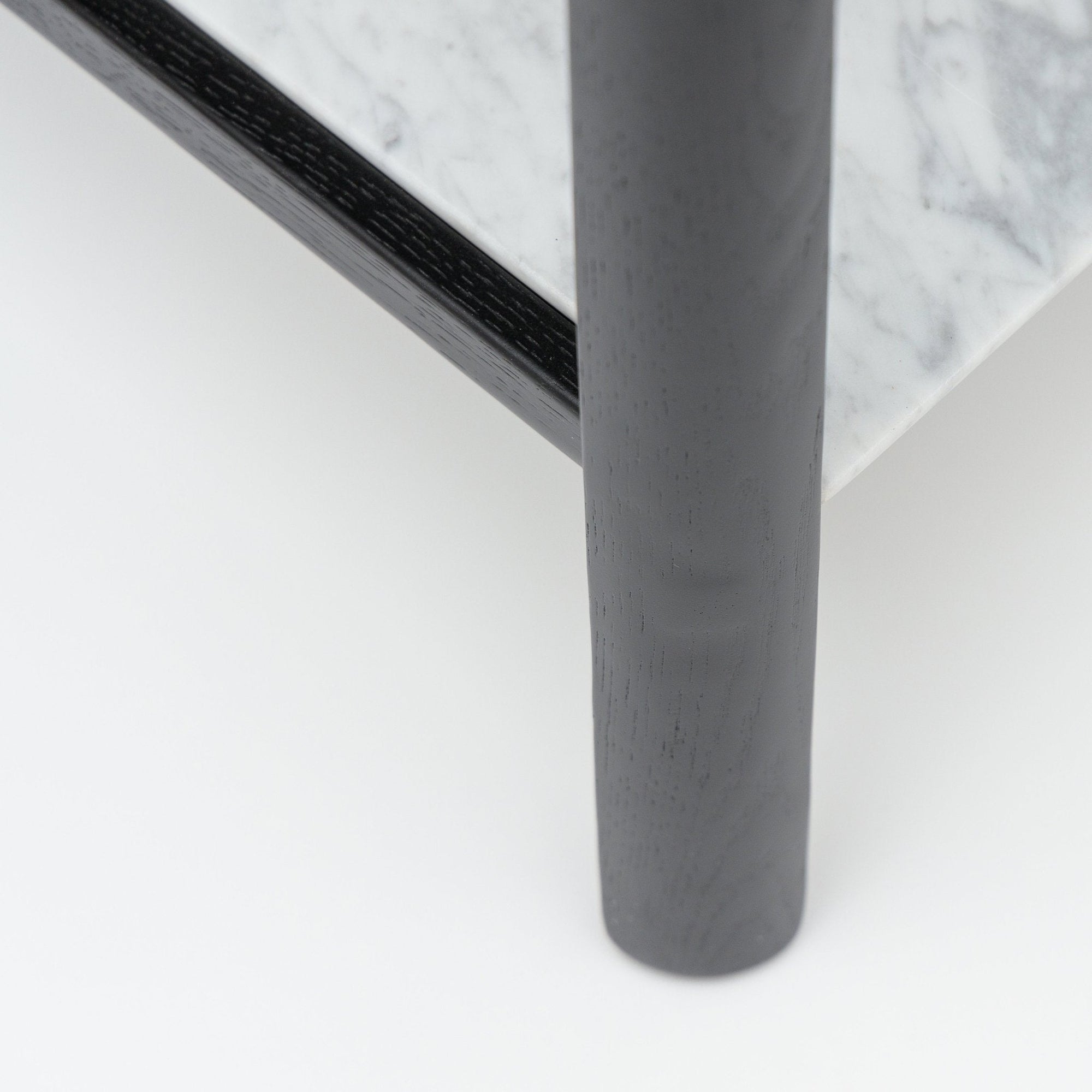 Close-up of the Nell Console by Wooden Stories: black oak edge, gray cylindrical leg, and polished white marble top with subtle veining—Scandinavian-inspired elegance set against a smooth white background.