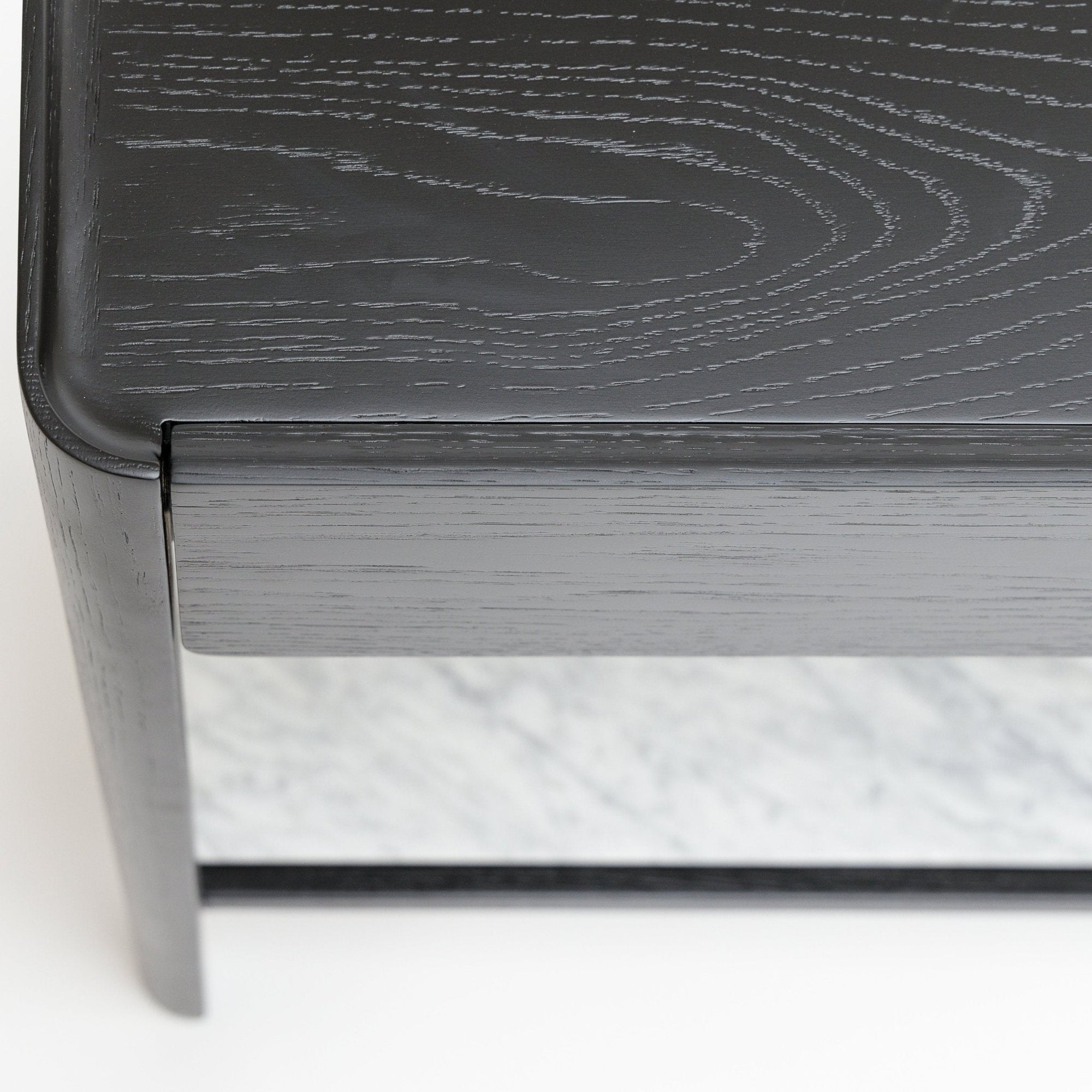 Close-up of the Nell Console by Wooden Stories, featuring black solid oak with visible wood grain. A white stone shelf sits beneath the tabletop, reflecting minimalist Scandinavian design influences.
