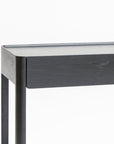 A close-up of the Nell Console by Wooden Stories in black oak with stone, featuring a minimalist rectangular top and straight legs, photographed against a plain white background to highlight its refined Scandinavian design.