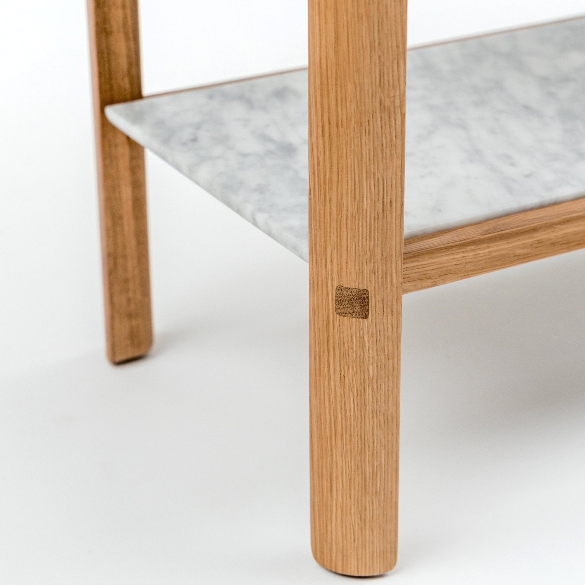 Close-up of the Nell Console by Wooden Stories, featuring a light oak leg and a lower shelf in gray-veined white stone. Set against a plain white background, the console showcases clean, Scandinavian-inspired lines.