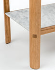 Close-up of the Nell Console by Wooden Stories, featuring a light oak leg and a lower shelf in gray-veined white stone. Set against a plain white background, the console showcases clean, Scandinavian-inspired lines.