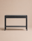 The Nell Console in Black Oak by Wooden Stories, from the Danish collection, is a minimalist piece featuring two drawers, a lower shelf, and rounded legs, styled against a solid neutral beige background.