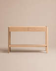 The Nell Console in Light Oak by Wooden Stories, featuring a minimalist Danish design with solid oak construction, two drawers, and an open lower shelf, is showcased against a plain beige background.