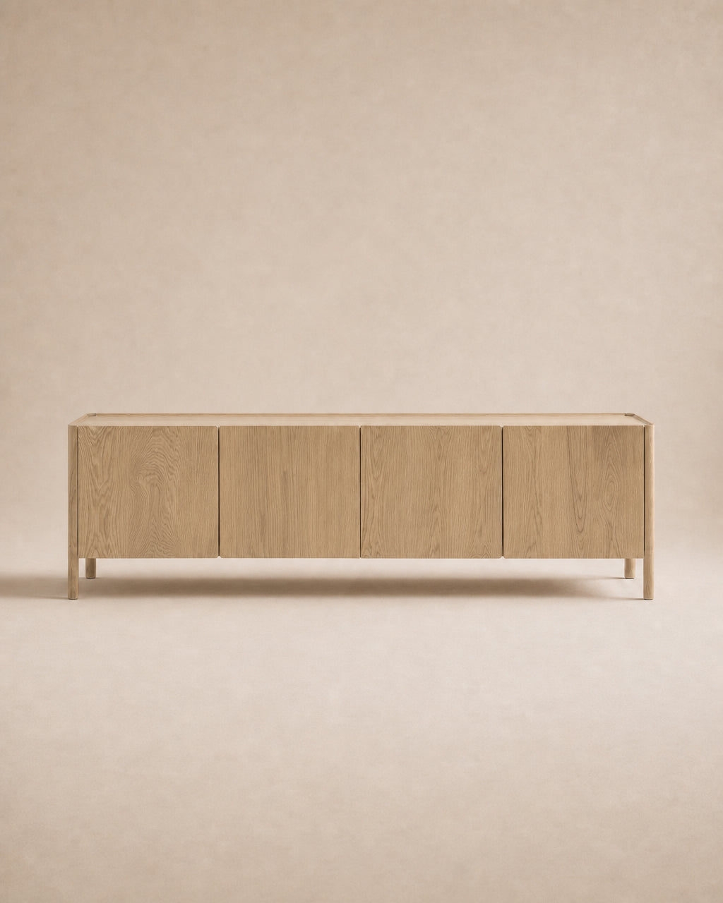 The Nell Sideboard | Blonde Oak by Wooden Stories is a minimalist wooden sideboard featuring four flat-panel doors, set against a beige background. Crafted from solid oak with a natural blonde finish, the cabinet showcases clean, straight lines and a modern, simple aesthetic inspired by Scandinavian design principles.