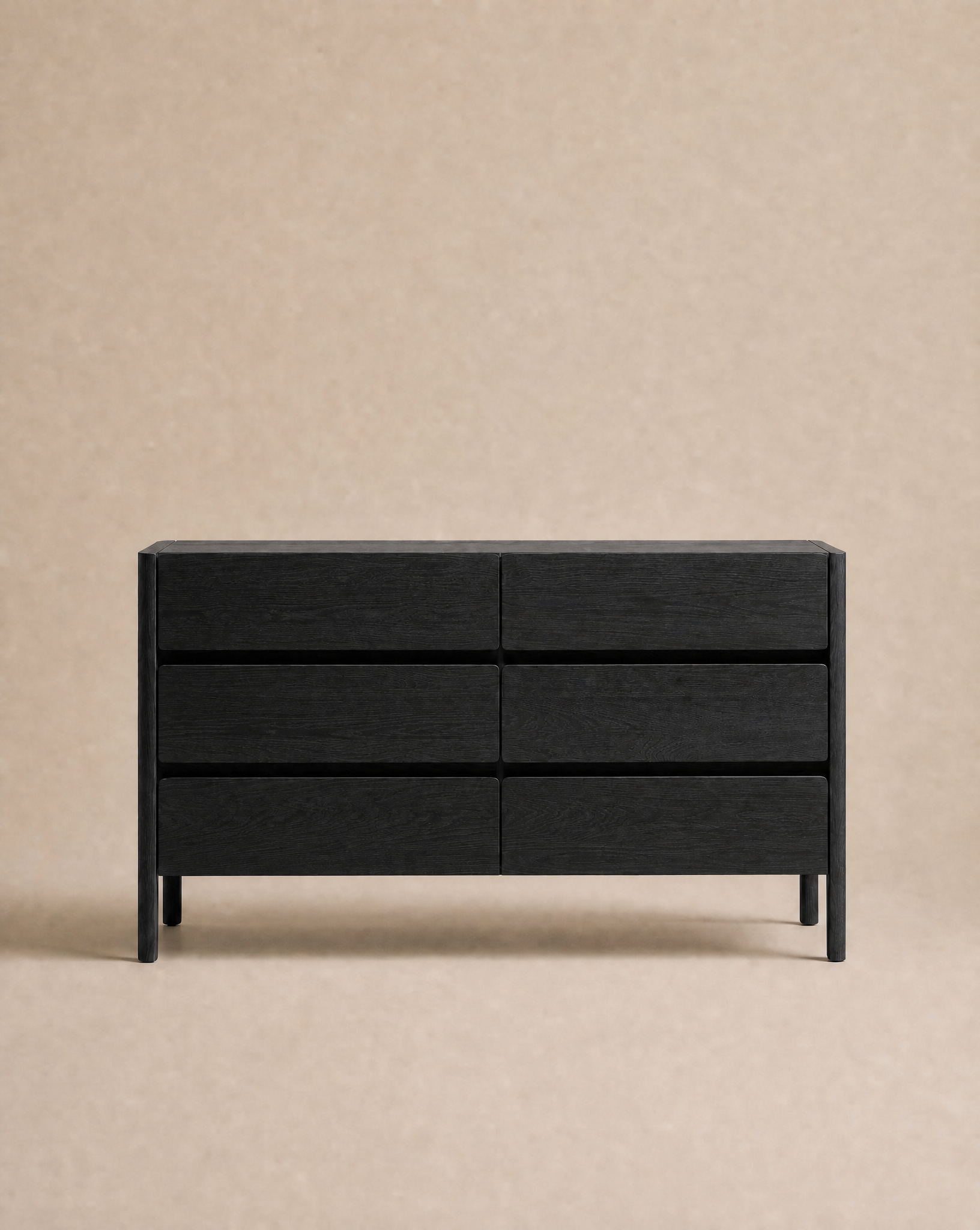 The Nell Wide Dresser by Wooden Stories, featuring six black wooden drawers, stands against a plain beige background, offering elegant bedroom storage with its classic design.