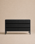 The Nell Wide Dresser by Wooden Stories, featuring six black wooden drawers, stands against a plain beige background, offering elegant bedroom storage with its classic design.