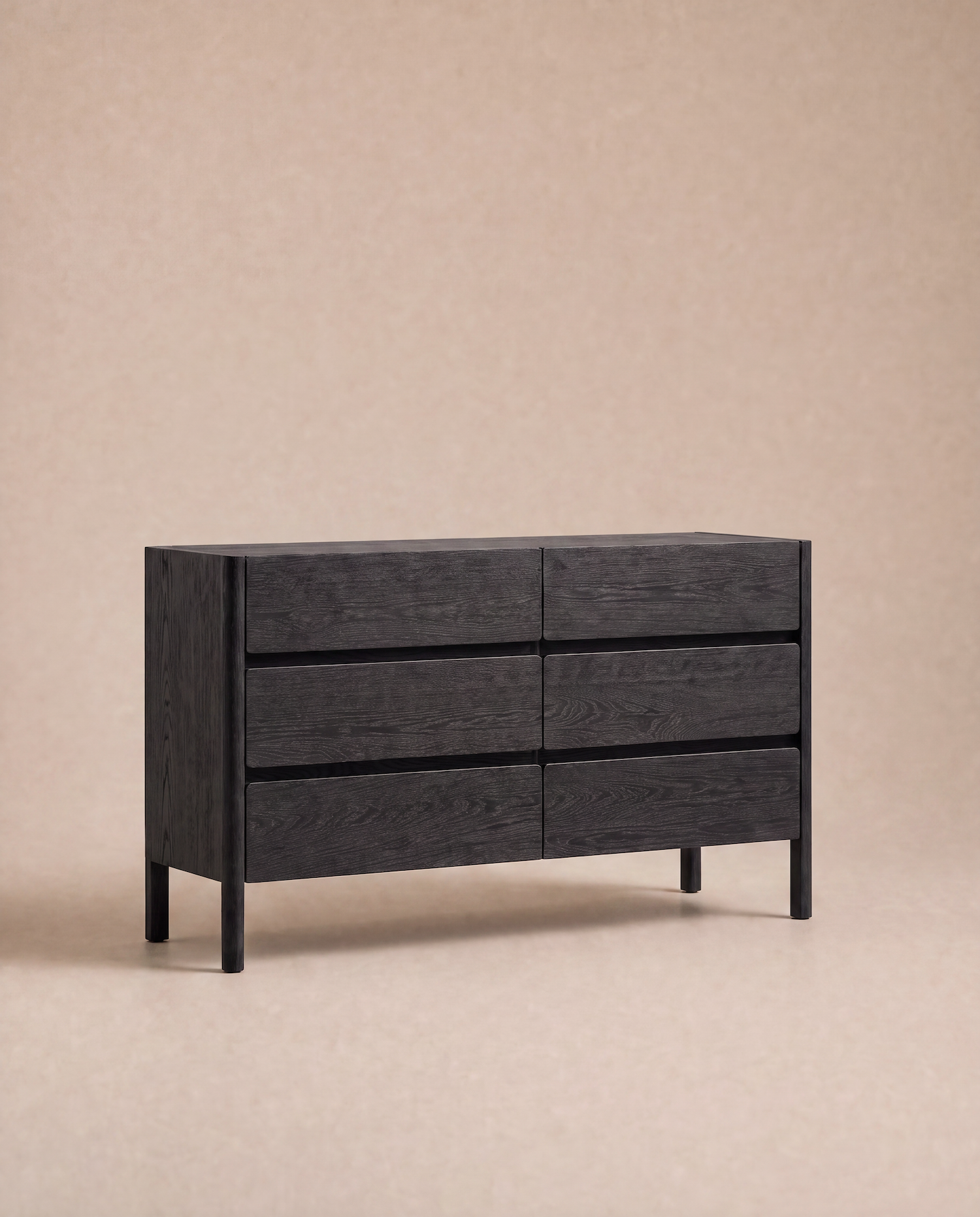 The Nell Wide Dresser by Wooden Stories from the Danish Collection is a modern black wooden dresser with six drawers, showcased on a light beige background. It features minimalist timber joinery, clean lines, and handle-free design, making it an ideal choice for stylish bedroom storage.