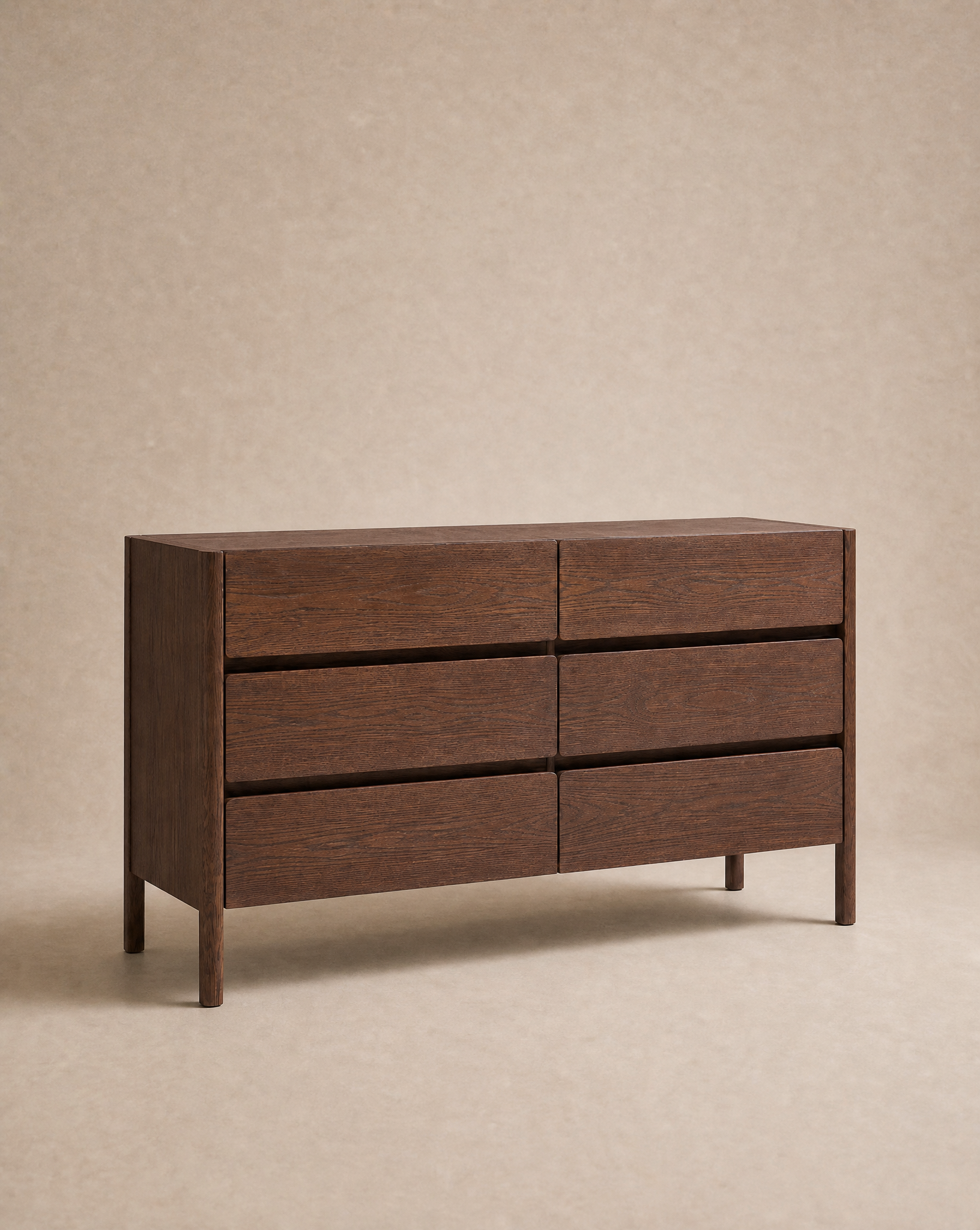 The Nell Wide Dresser by Wooden Stories is a modern dark wood piece from the Danish Collection, featuring six drawers and set against a plain beige background. Its simple rectangular silhouette showcases clean lines with no visible handles and premium metal runners for seamless drawer operation—making it an ideal choice for stylish bedroom storage.