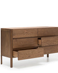 The Wooden Stories Nell Wide Dresser showcases minimalist design and fine timber joinery as part of the Danish Collection. Featuring six wooden drawers—three partially open—it stands on four legs against a plain white background, offering a stylish and practical bedroom storage solution.