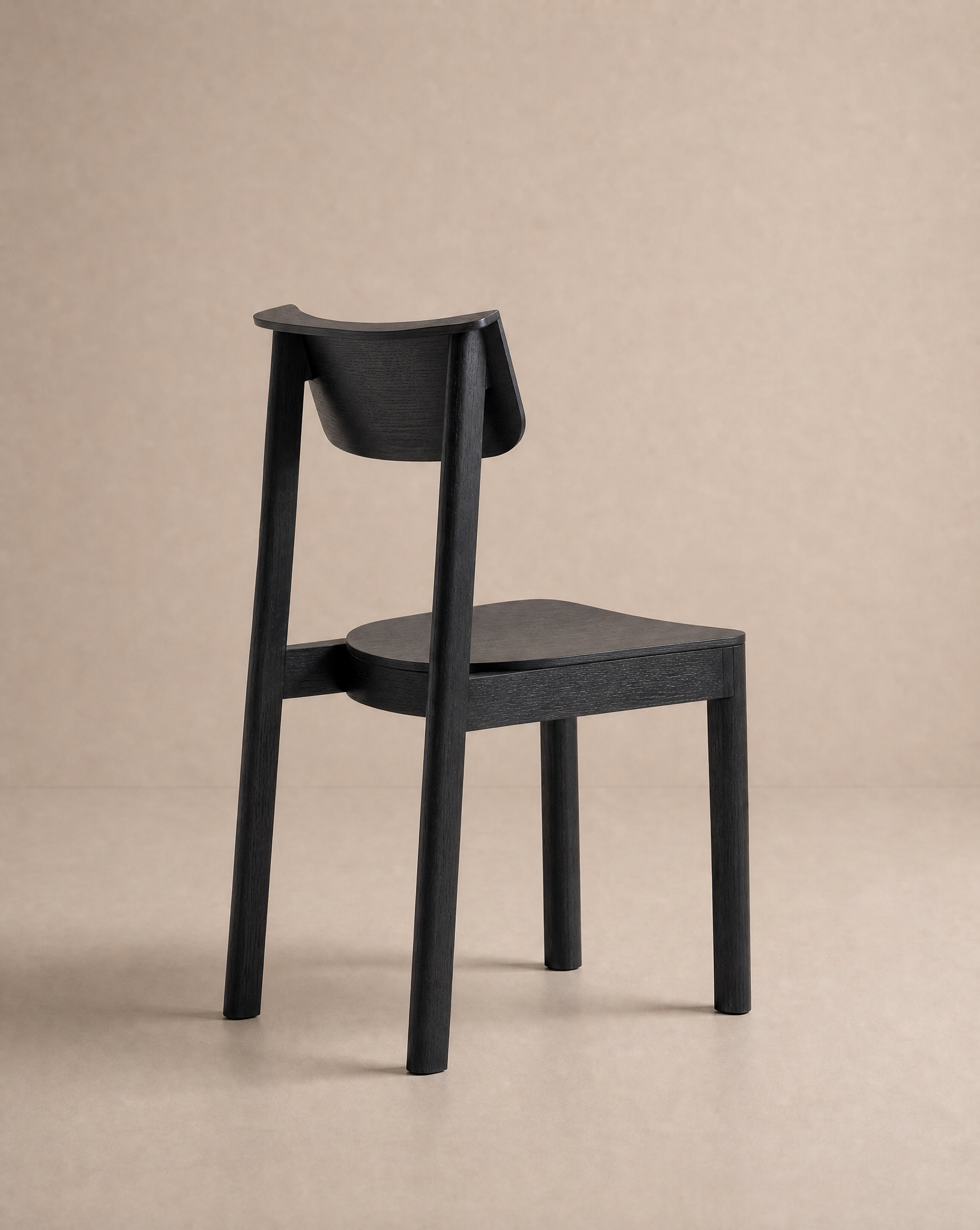 The Noki Dining Chair | Wood by Wooden Stories features a modern, minimalist solid wood design with a curved backrest, shown from behind at an angle against a plain beige background.