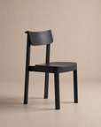 The Noki Dining Chair | Wood by Wooden Stories is a minimalist, contract-grade piece made from solid wood, featuring a curved backrest and seat with clean lines and no visible upholstery against a beige background.