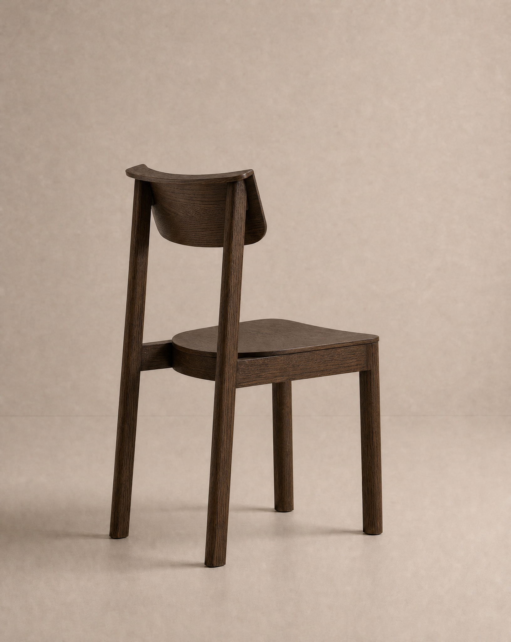 The Noki Dining Chair | Wood by Wooden Stories is a contract-grade solid wood chair with a flat seat and curved backrest, displayed from behind at an angle against a neutral beige background.